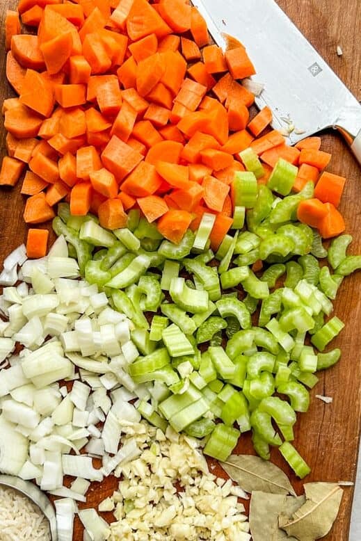 chopped carrots, celery, onion, garlic, bay leaves and rice on a cutting board