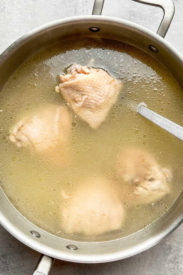 Bone-in and skin-on chicken thighs being boiled to make the base of the avgolemono soup