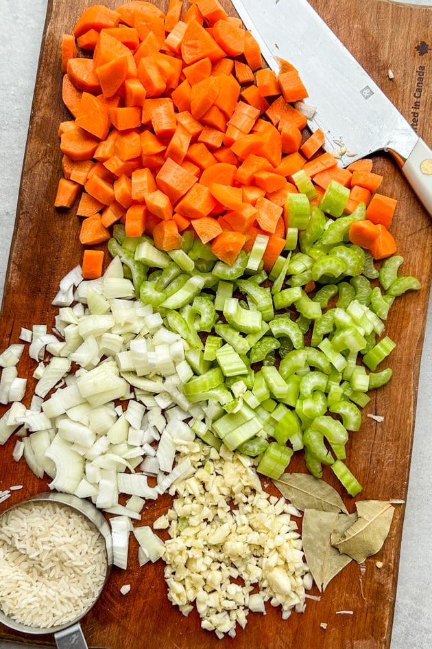 chopped carrots, celery, onion, garlic, bay leaves and rice on a cutting board